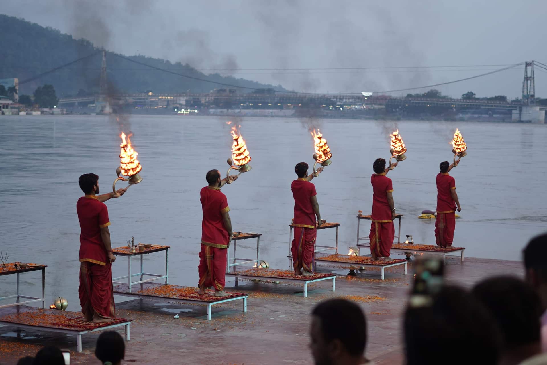 Priests in red robes holding tiered flaming lamps during Ganga aarti on a riverside ghat in Rishikesh