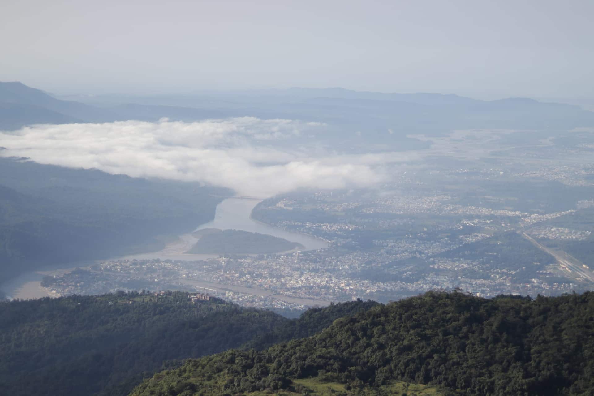 Forested Himalayan hills falling to the Ganga winding past Rishikesh, with low cloud in the valley